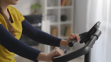 student-woman-is-training-with-stationary-bike-in-room-spinning-pedals-closeup-view-of-face-and-body-sport-and-fitness-at-home